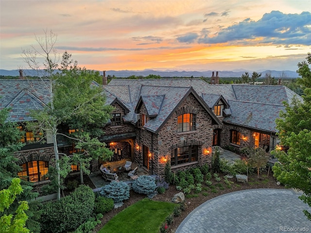 view of front of home with a high end roof, stone siding, a chimney, a mountain view, and a patio