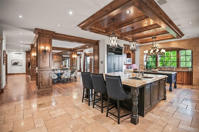 kitchen featuring a sink, a large island with sink, stone tile flooring, a chandelier, and recessed lighting