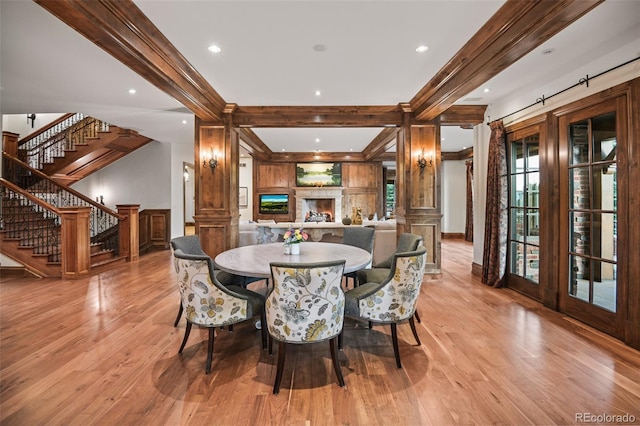 dining area with light wood-type flooring, stairway, beam ceiling, a warm lit fireplace, and recessed lighting