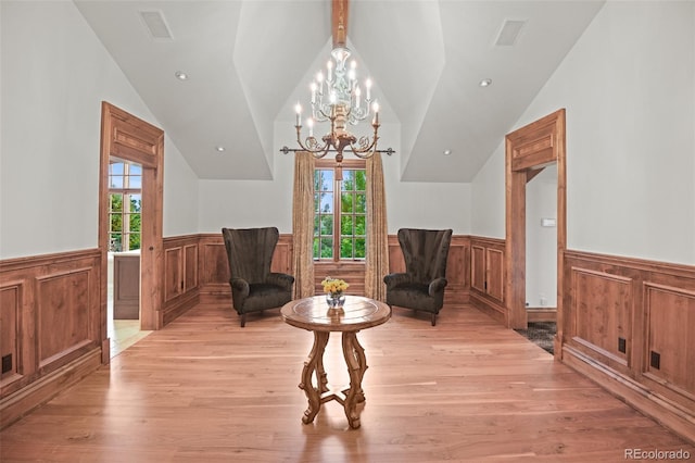living area featuring wainscoting, vaulted ceiling, light wood finished floors, a chandelier, and plenty of natural light