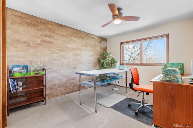 carpeted home office with ceiling fan and brick wall