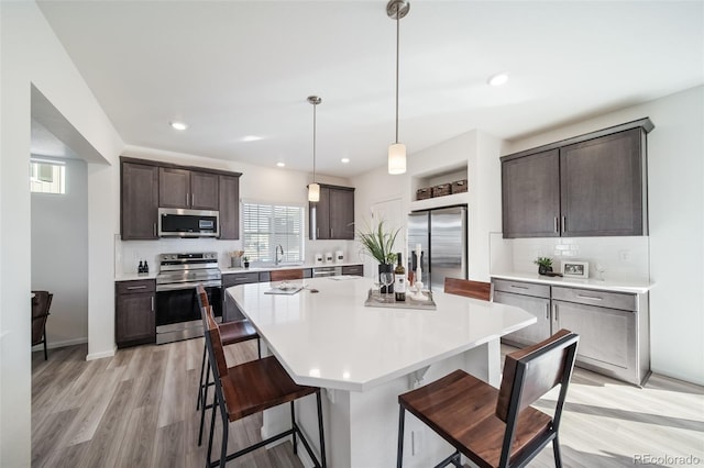 kitchen with pendant lighting, a breakfast bar, a center island, dark brown cabinets, and stainless steel appliances