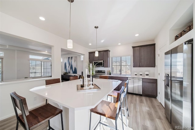 kitchen featuring a center island, hanging light fixtures, a kitchen bar, dark brown cabinetry, and stainless steel appliances