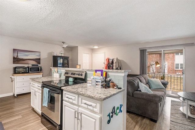 kitchen with light wood finished floors, appliances with stainless steel finishes, white cabinetry, open floor plan, and a center island