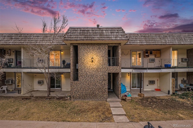 exterior space with brick siding, stucco siding, mansard roof, and a patio