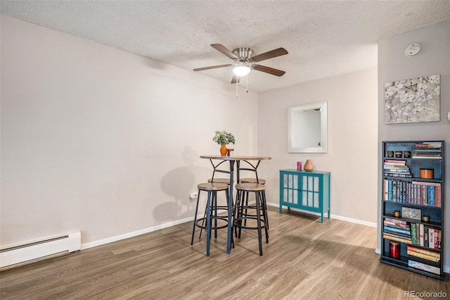 dining room featuring wood finished floors, baseboards, ceiling fan, a textured ceiling, and a baseboard heating unit