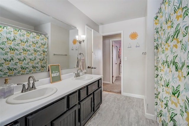 full bath with wood finished floors, a sink, baseboards, and double vanity