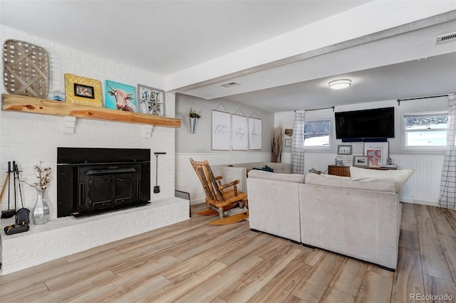 living area with a wainscoted wall, a brick fireplace, wood finished floors, and visible vents