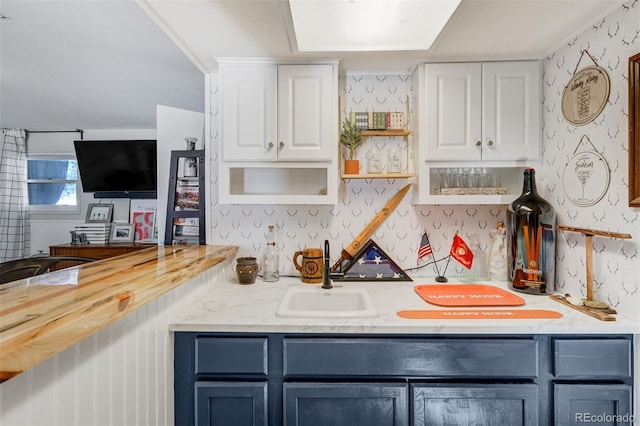 kitchen featuring blue cabinets, a sink, white cabinetry, and wallpapered walls