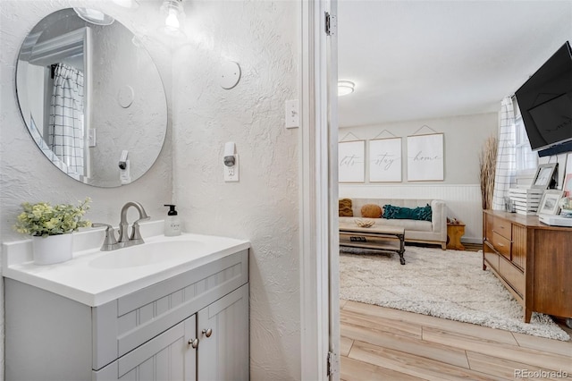 bathroom featuring a wainscoted wall, a textured wall, vanity, and wood finished floors