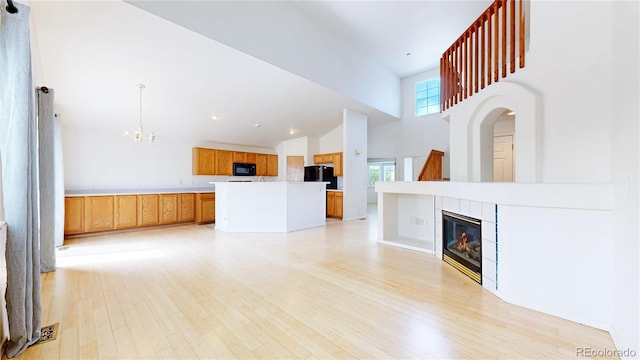2314 Flagstaff Dr, Longmont, CO 80504 - unfurnished living room featuring a chandelier, high vaulted ceiling, a tile fireplace, and light wood-style flooring