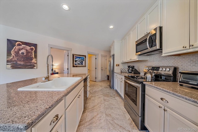 kitchen with sink, white cabinetry, a kitchen island with sink, stainless steel appliances, and light stone counters