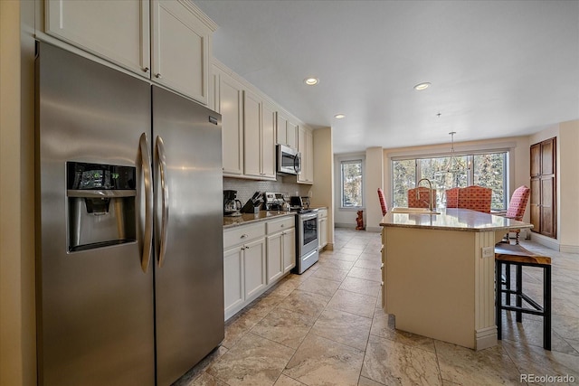 kitchen with white cabinets, a kitchen bar, decorative light fixtures, stainless steel appliances, and a center island with sink