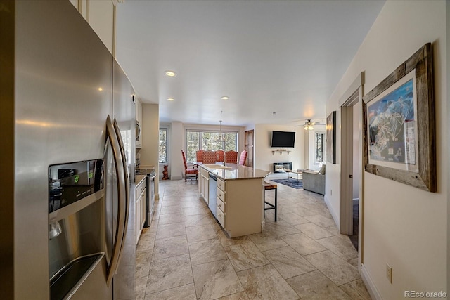 kitchen with ceiling fan, appliances with stainless steel finishes, a center island, a breakfast bar, and sink