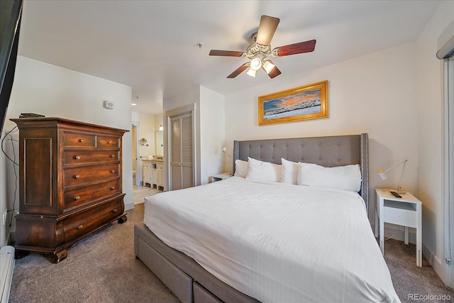 carpeted bedroom with a closet, ensuite bathroom, baseboard heating, and ceiling fan