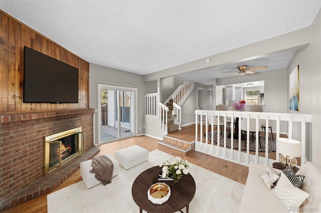 living room featuring ceiling fan, wood walls, wood-type flooring, a textured ceiling, and a fireplace