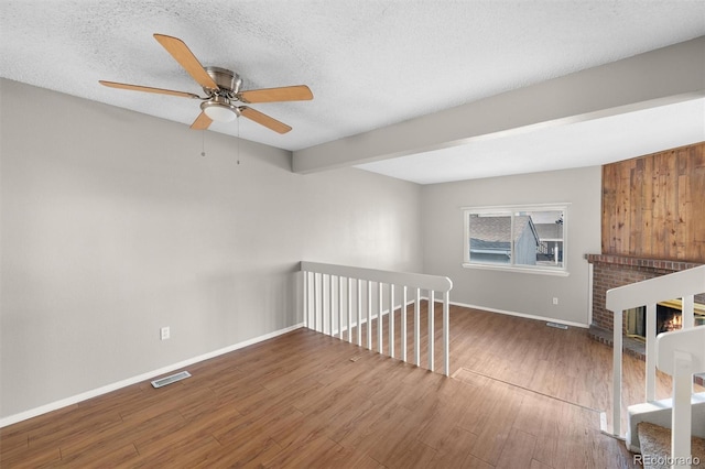 empty room with a brick fireplace, hardwood / wood-style floors, a textured ceiling, and ceiling fan