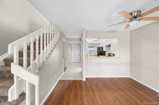 unfurnished living room featuring ceiling fan, a textured ceiling, and light hardwood / wood-style flooring