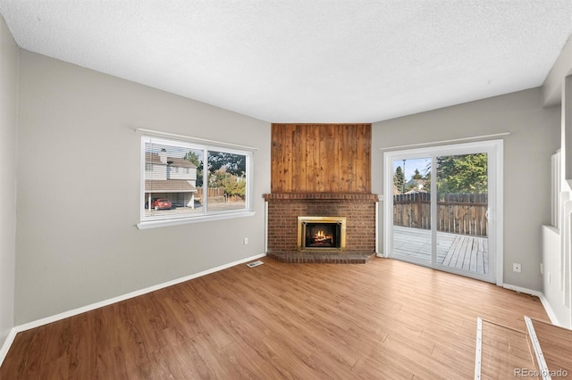 unfurnished living room with a brick fireplace, light hardwood / wood-style flooring, and a textured ceiling