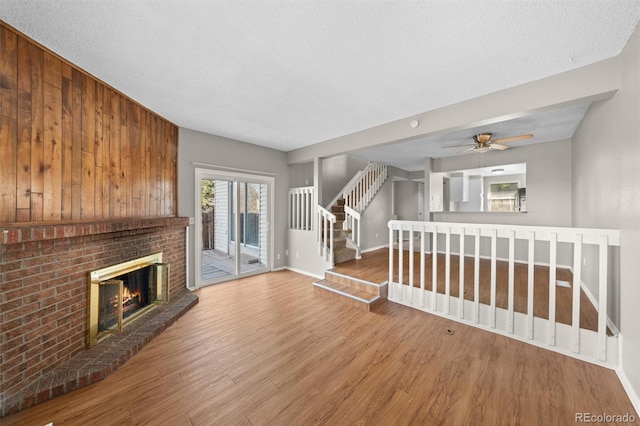 unfurnished living room featuring a brick fireplace, a textured ceiling, hardwood / wood-style floors, and ceiling fan