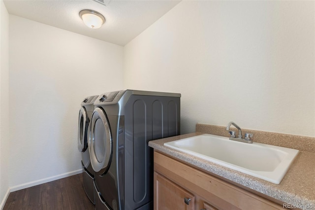 laundry room featuring dark wood finished floors, independent washer and dryer, a sink, baseboards, and cabinet space