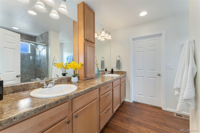 full bath with visible vents, a sink, double vanity, wood finished floors, and a stall shower