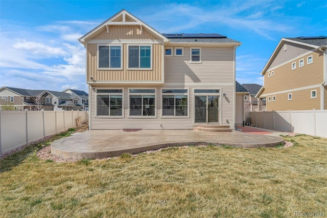 rear view of house with a patio, entry steps, a fenced backyard, a yard, and roof mounted solar panels