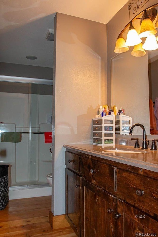 bathroom with a shower with shower door, hardwood / wood-style floors, toilet, and vanity with extensive cabinet space