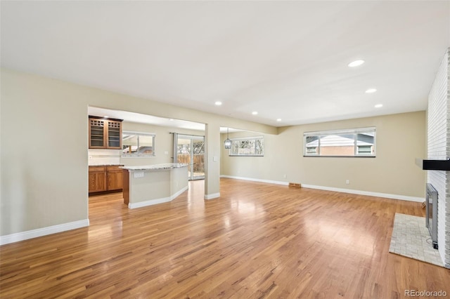 unfurnished living room featuring light wood-style flooring, a brick fireplace, and baseboards