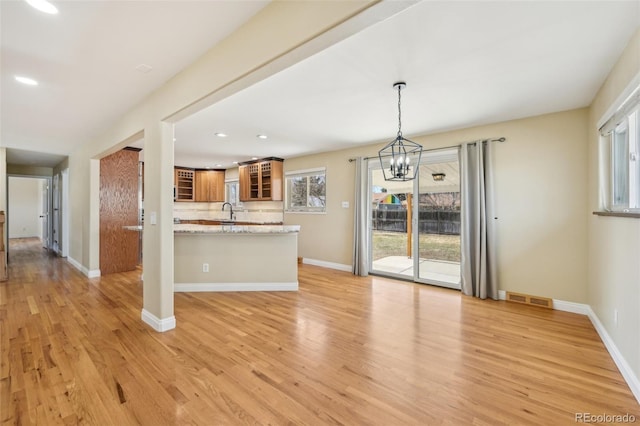 kitchen with decorative backsplash, glass insert cabinets, light wood-style floors, and visible vents