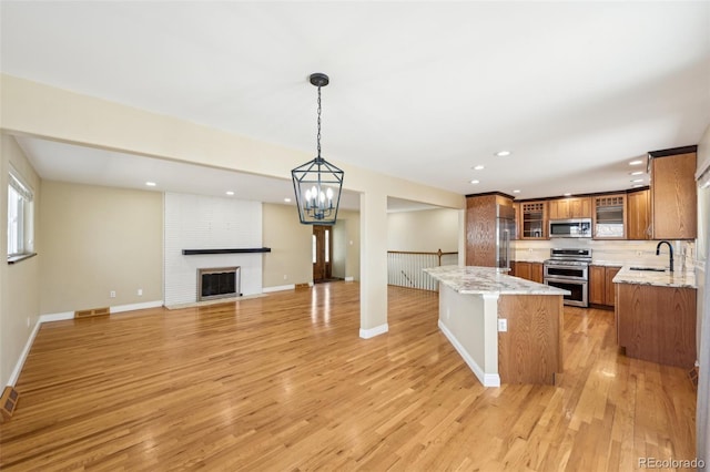 kitchen with light stone counters, brown cabinetry, stainless steel appliances, a brick fireplace, and light wood-type flooring