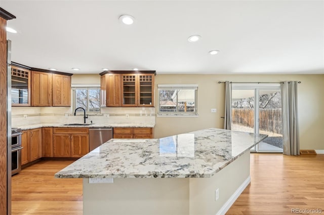 kitchen featuring brown cabinets, a sink, backsplash, stainless steel appliances, and light wood-style floors