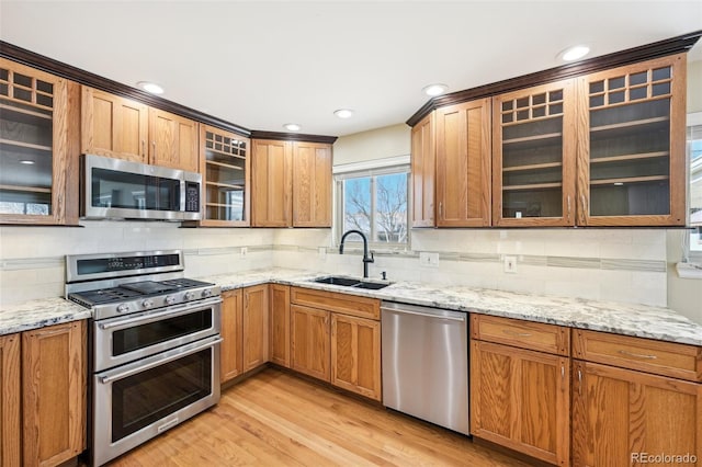 kitchen featuring decorative backsplash, a sink, stainless steel appliances, light wood-style floors, and glass insert cabinets