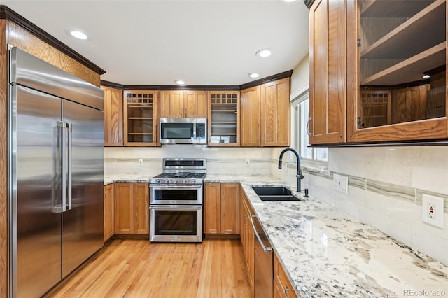 kitchen with light stone countertops, light wood-style flooring, a sink, appliances with stainless steel finishes, and brown cabinets