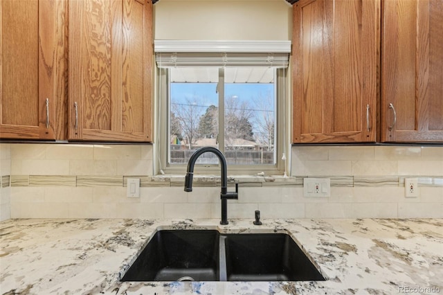 kitchen with a sink, light stone counters, tasteful backsplash, and brown cabinetry