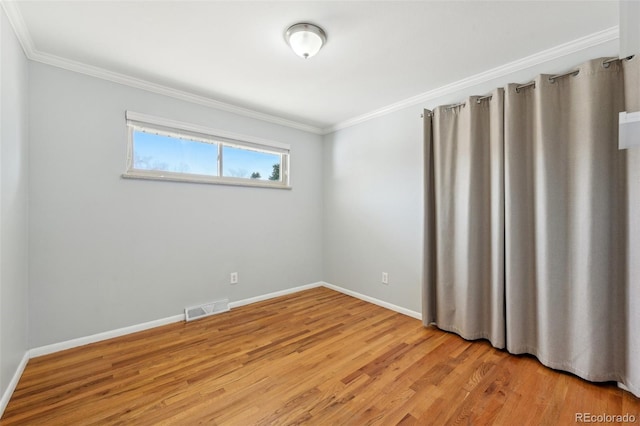 empty room with light wood-type flooring, visible vents, baseboards, and crown molding