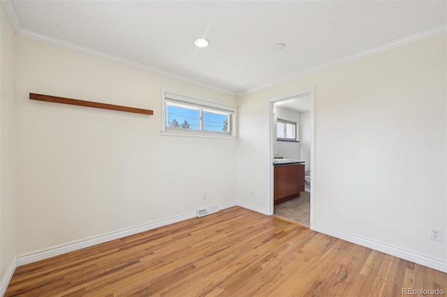 spare room with visible vents, light wood-style flooring, baseboards, and ornamental molding