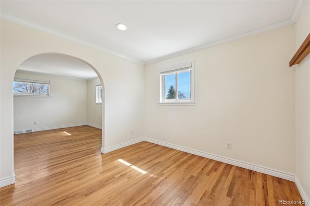 empty room with crown molding, baseboards, arched walkways, and light wood finished floors