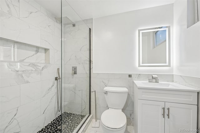 full bath featuring a marble finish shower, tile walls, toilet, wainscoting, and vanity