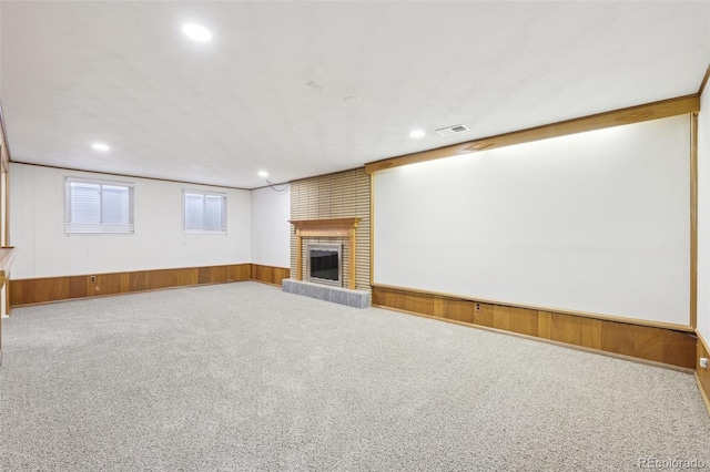 unfurnished living room featuring visible vents, carpet floors, a brick fireplace, and a wainscoted wall