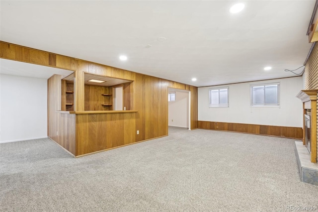 unfurnished living room with a fireplace with raised hearth, recessed lighting, wood walls, and carpet floors