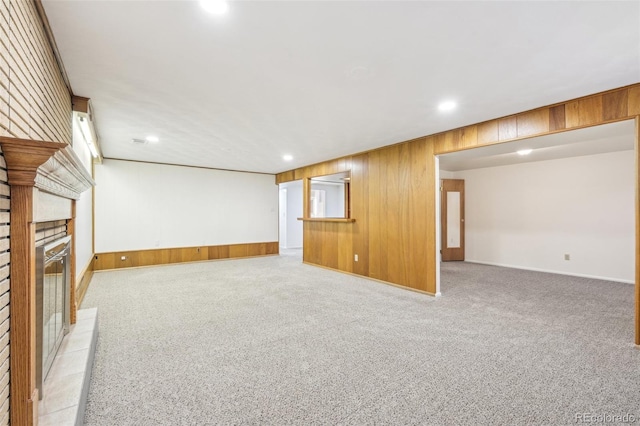 unfurnished living room featuring a glass covered fireplace, wooden walls, and light colored carpet