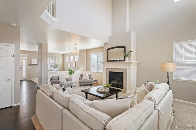 living area with baseboards, dark wood-style flooring, a towering ceiling, and a tiled fireplace