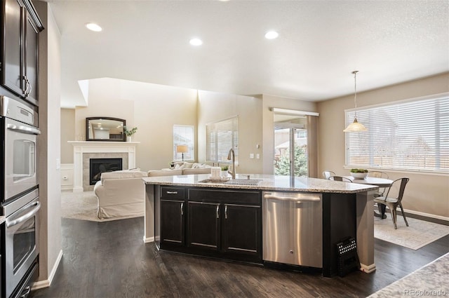 kitchen with a sink, decorative light fixtures, dark wood-style floors, appliances with stainless steel finishes, and a fireplace