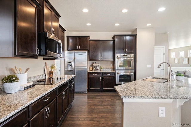 kitchen featuring a sink, stainless steel appliances, light stone countertops, and dark wood finished floors