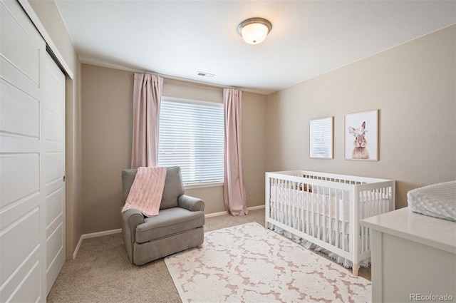 bedroom with visible vents, light carpet, a crib, a closet, and baseboards