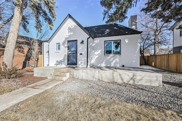 view of front facade featuring a patio, brick siding, a chimney, and fence