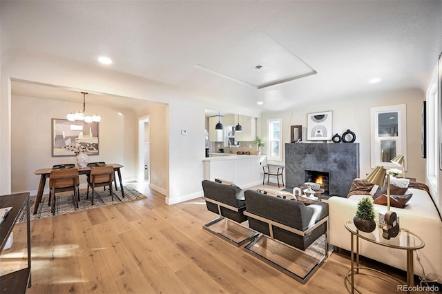 living room with light wood-type flooring, recessed lighting, an inviting chandelier, a fireplace, and baseboards