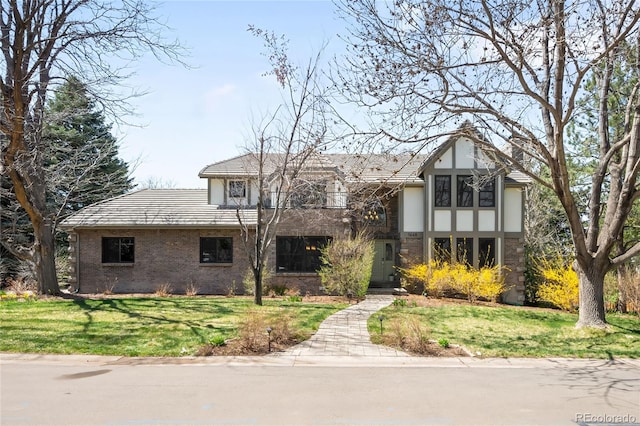 tudor home featuring brick siding, a front yard, and stucco siding