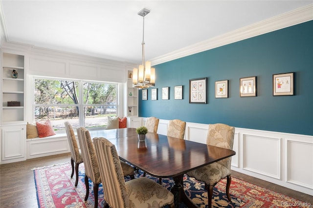 dining space with built in shelves, a chandelier, wood finished floors, a decorative wall, and ornamental molding